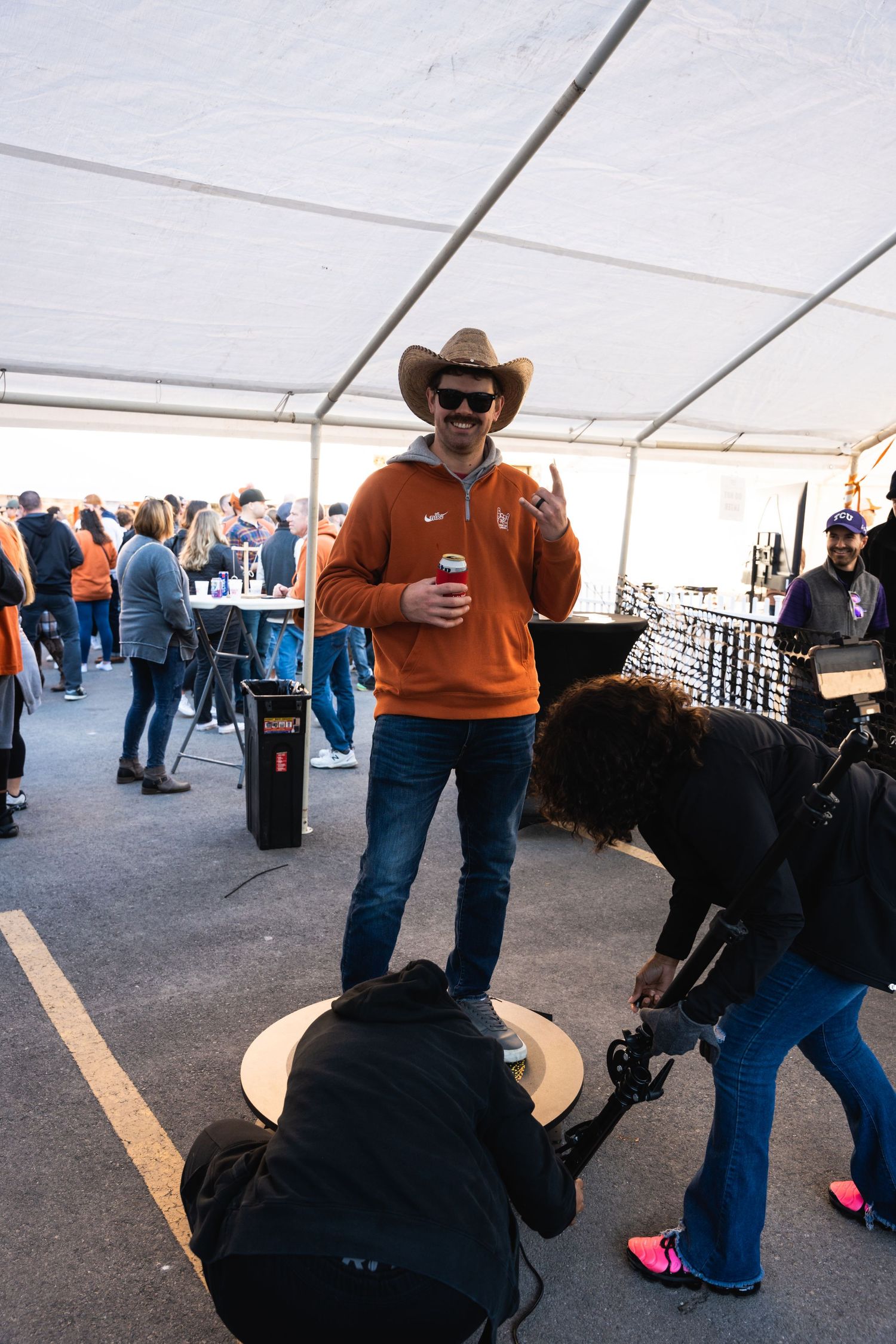 A person in Texas Longhorns gear poses under a white tent while photographers capture the moment.