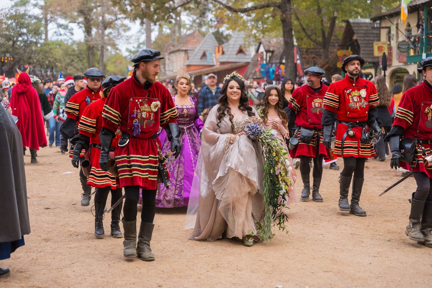 A royal procession with guards in red uniforms escorting a princess through a renaissance festival.