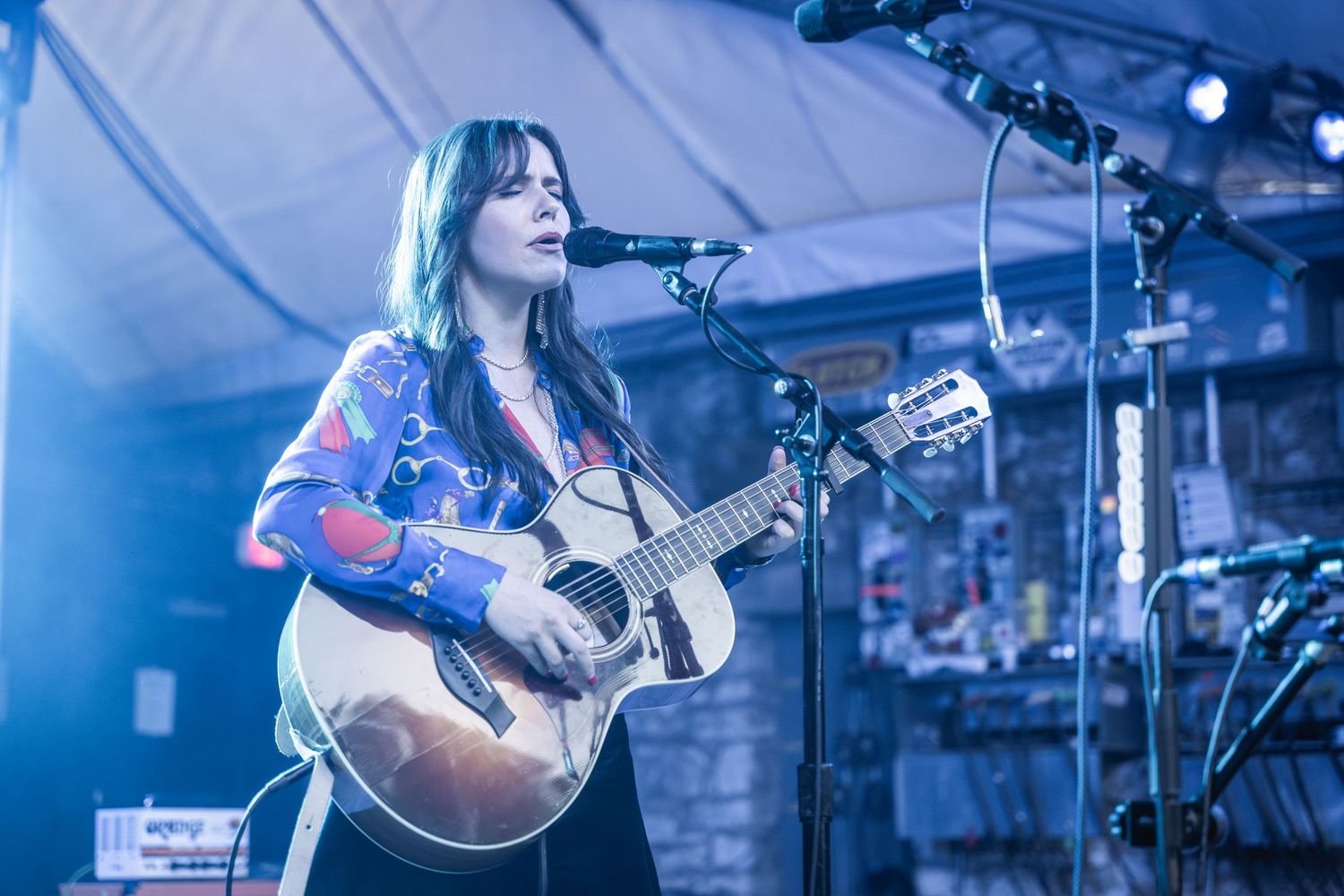 Musician performing with acoustic guitar on stage under blue lighting.