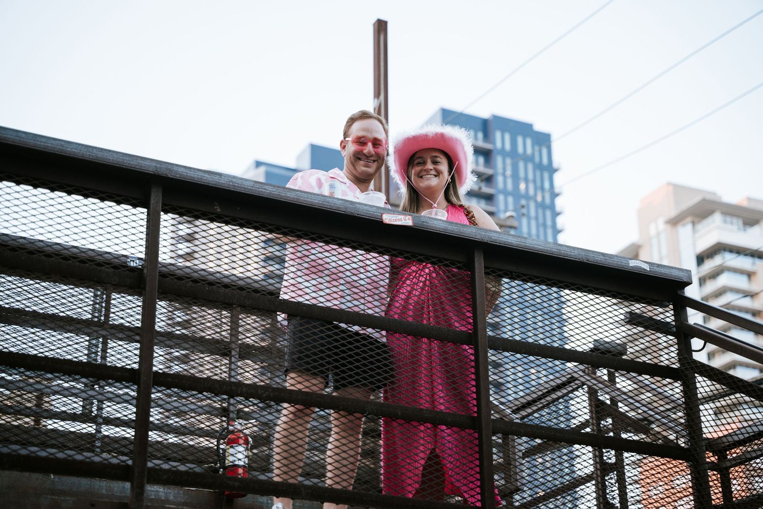 A couple stands on an industrial-style balcony overlooking an urban cityscape.