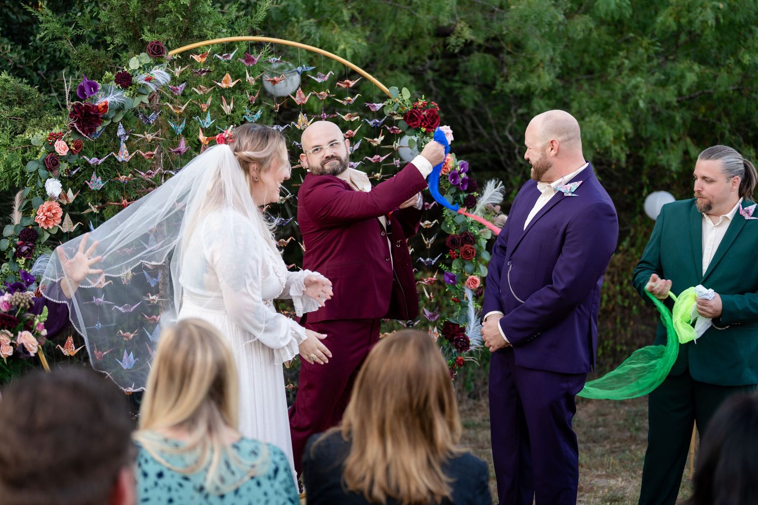 Wedding ceremony under arch with paper cranes and floral decorations in outdoor garden setting.