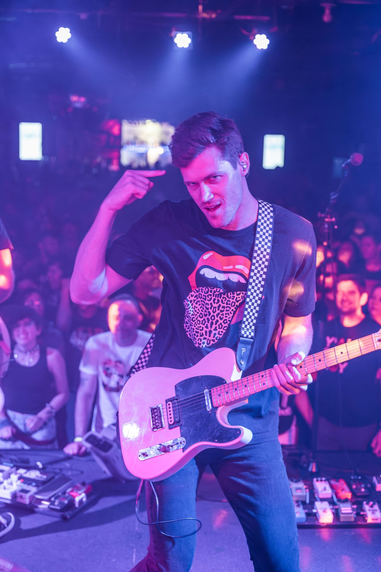 Guitarist performing on stage with pink and purple concert lighting.