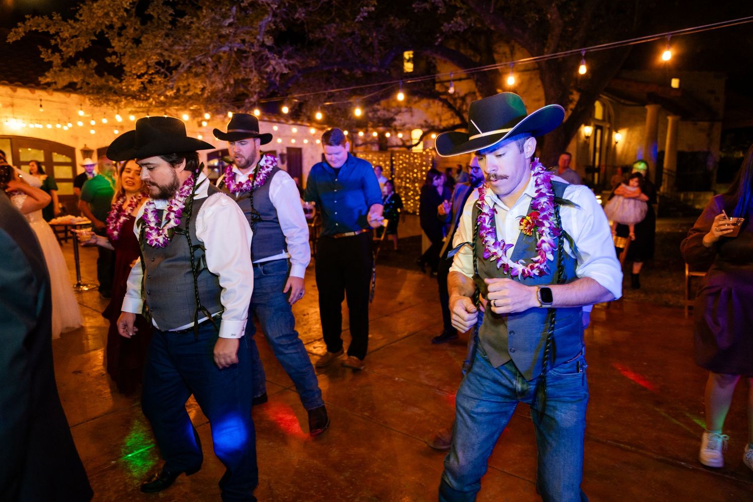 People dancing at a western-themed party with string lights and colorful illumination.