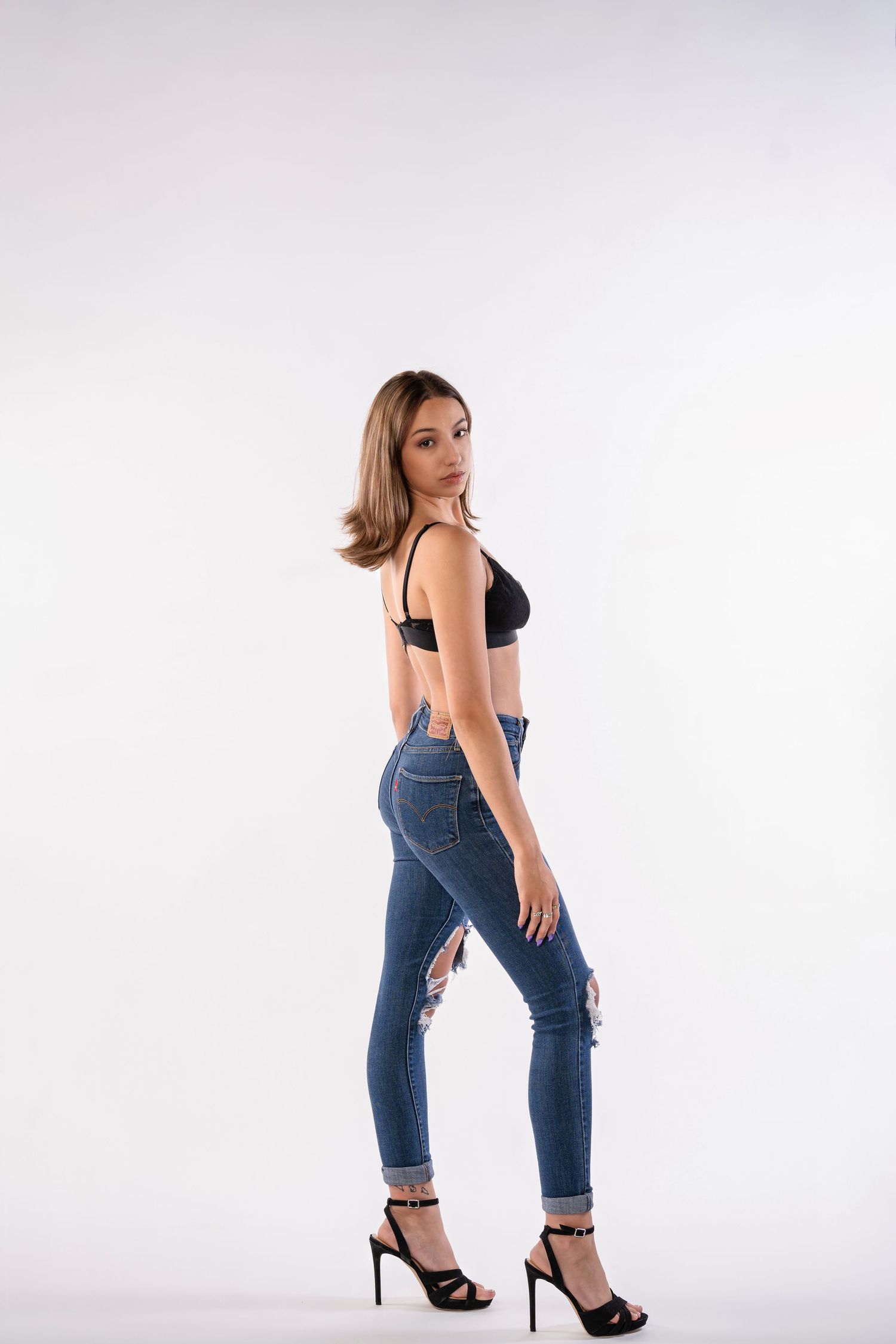 Fashion portrait of model in crop top and jeans with high heels against white background.