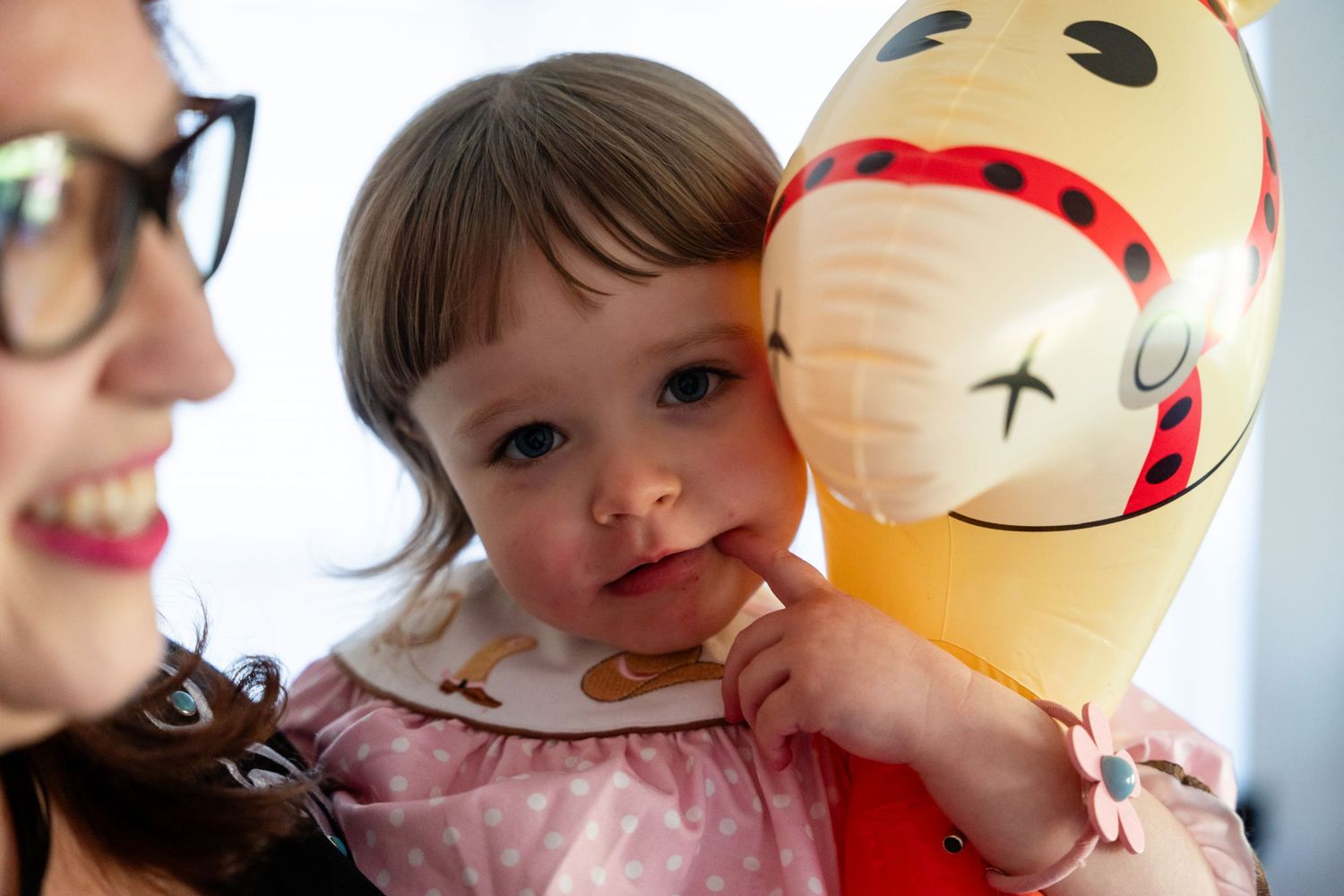 A young child holding a large plush character toy while being held by someone wearing glasses.