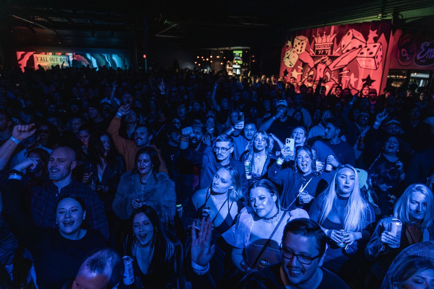 Concert crowd illuminated by blue lighting at packed indoor music venue.