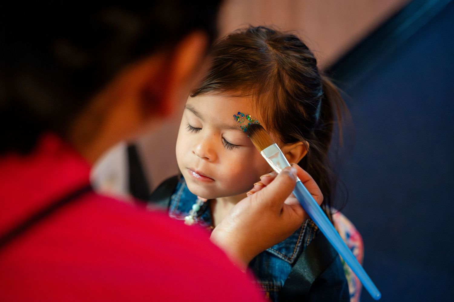 A child receives delicate face painting art with a small brush at close range.