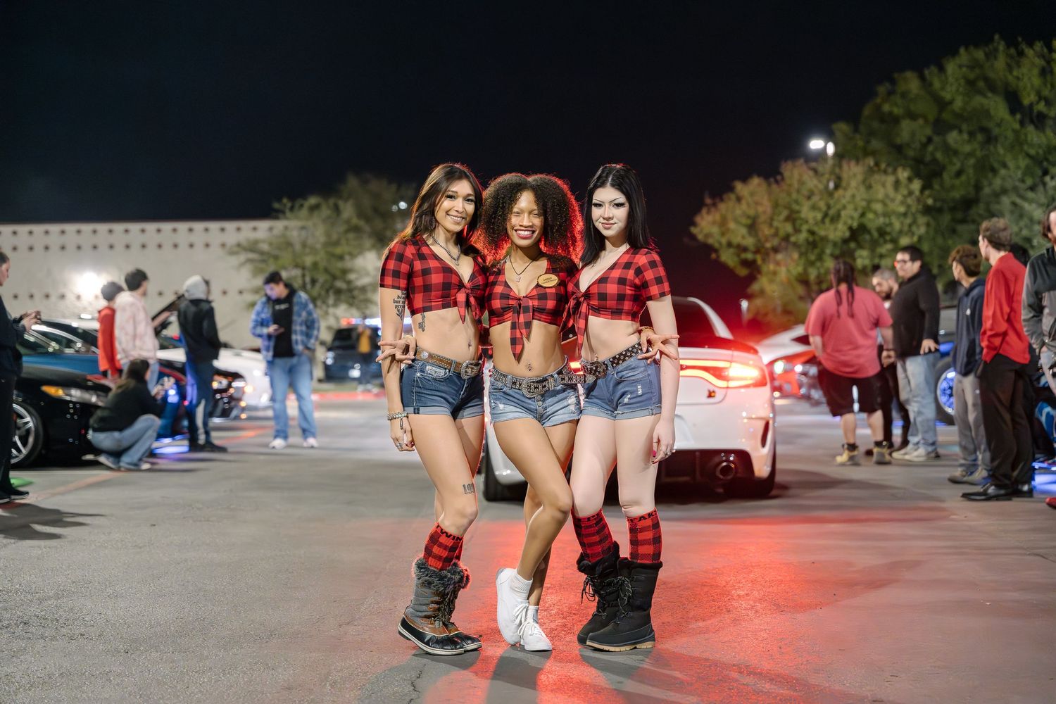 Nighttime car meet scene with red and plaid western style outfits.