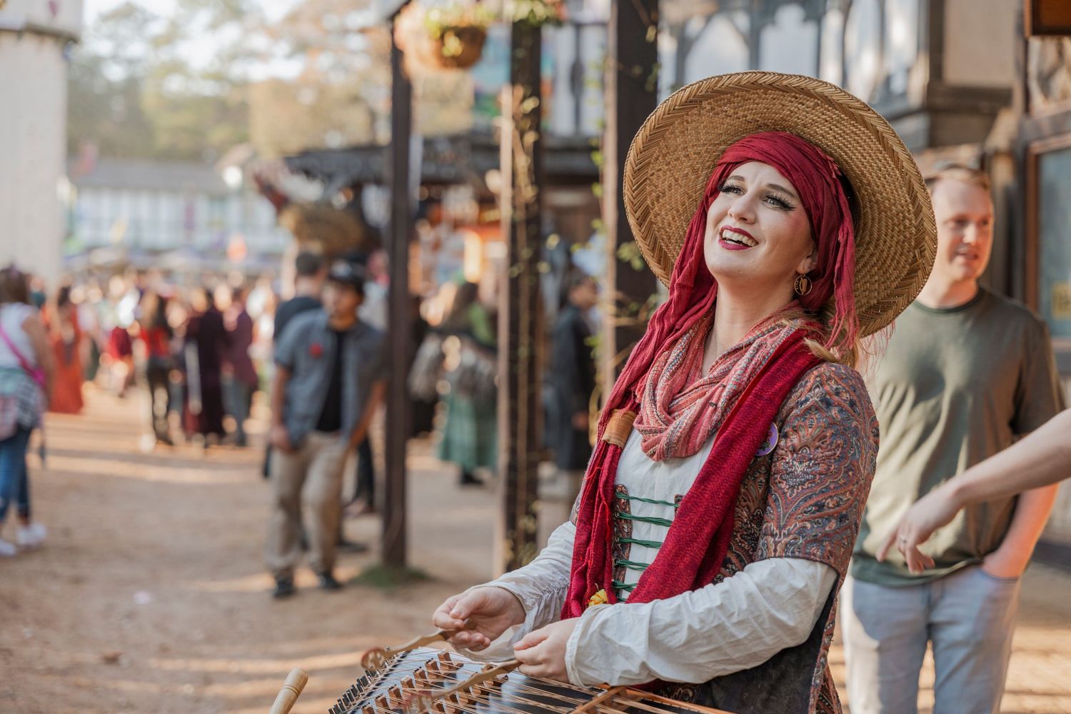 A performer in renaissance costume with a straw hat at an outdoor festival.