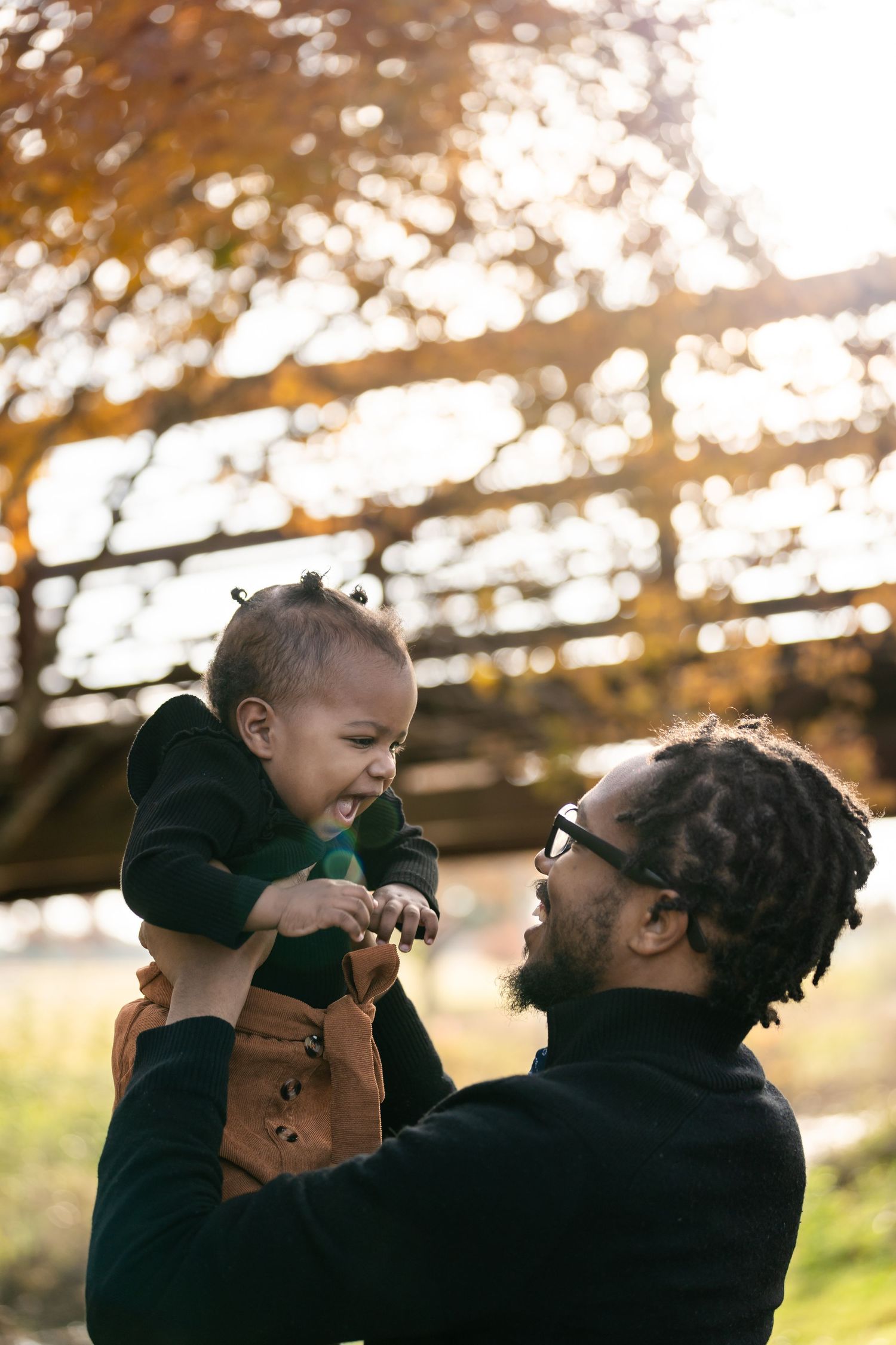 A joyful outdoor moment captured in golden sunlight beneath a wooden structure.