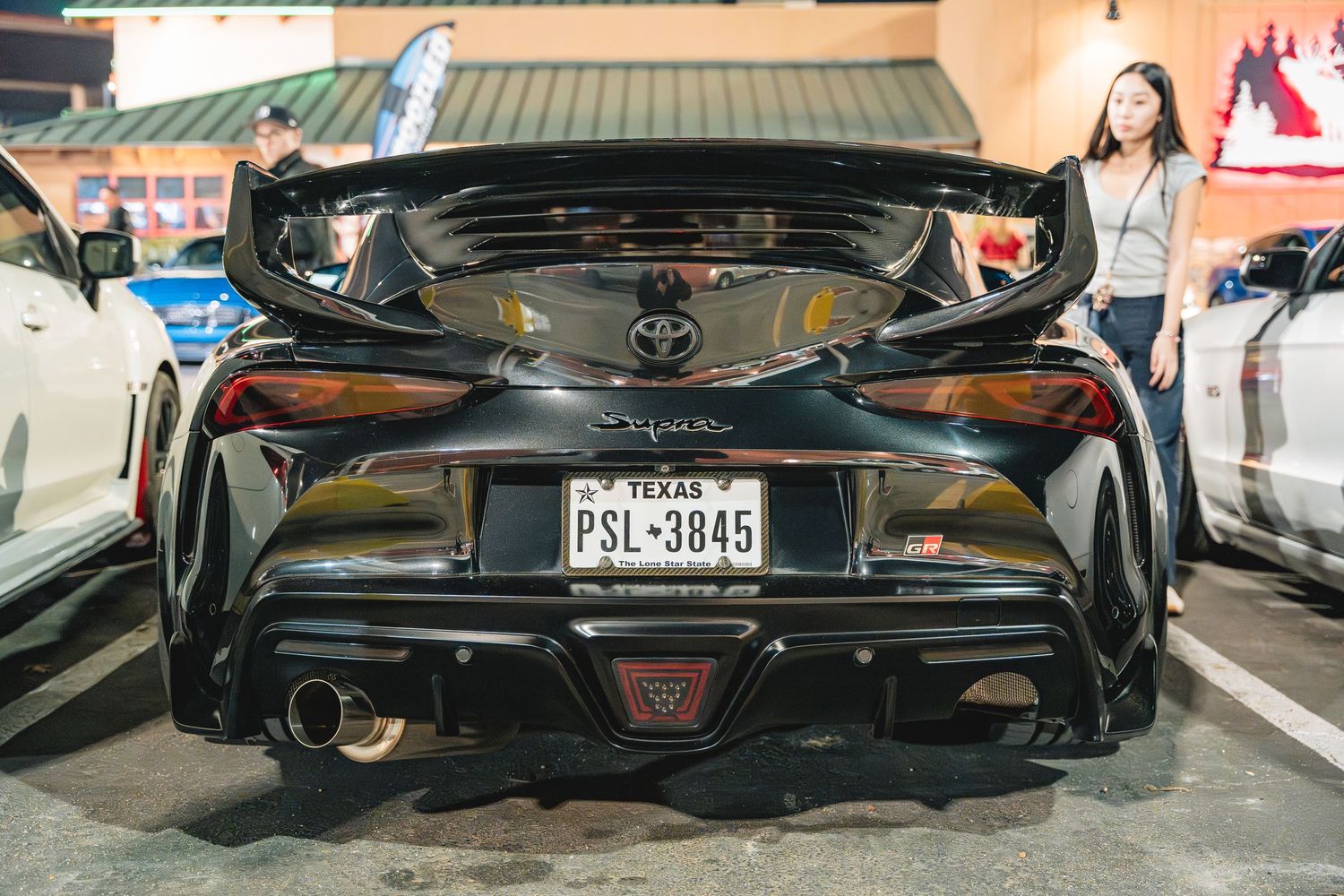 Rear view of a black Toyota GR Supra with custom exhaust and license plate.