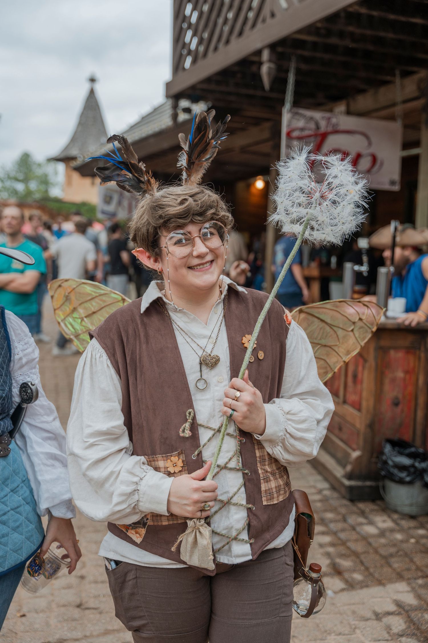 Fantasy cosplayer with fairy wings and antlers holding a decorative wand at renaissance faire.