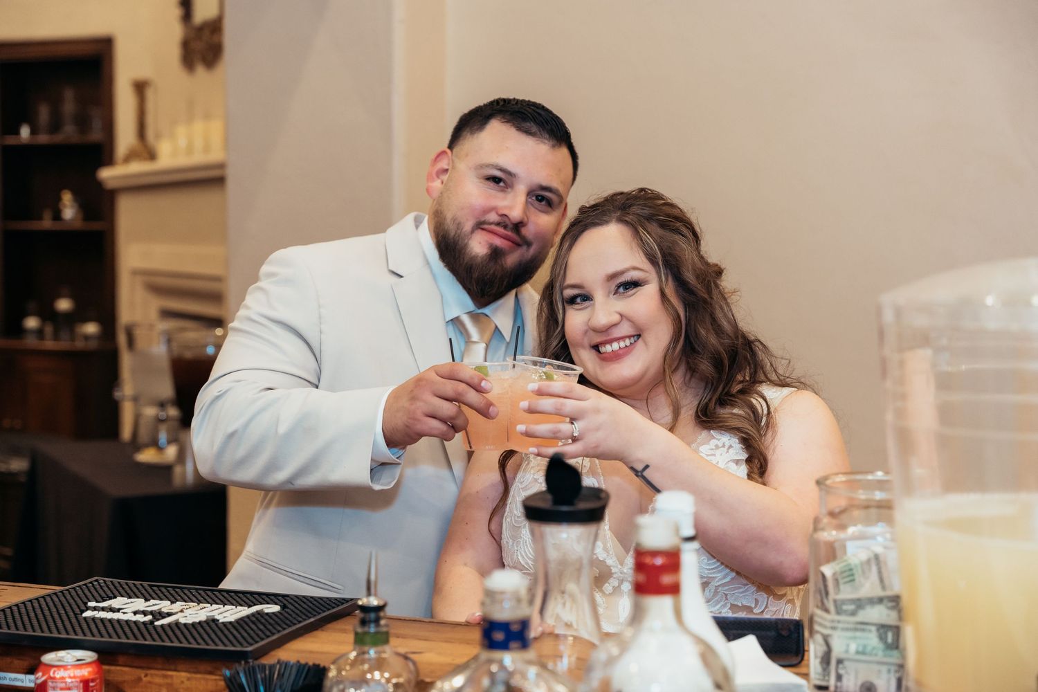 Newlyweds toast at their reception table surrounded by drinks and decorations.