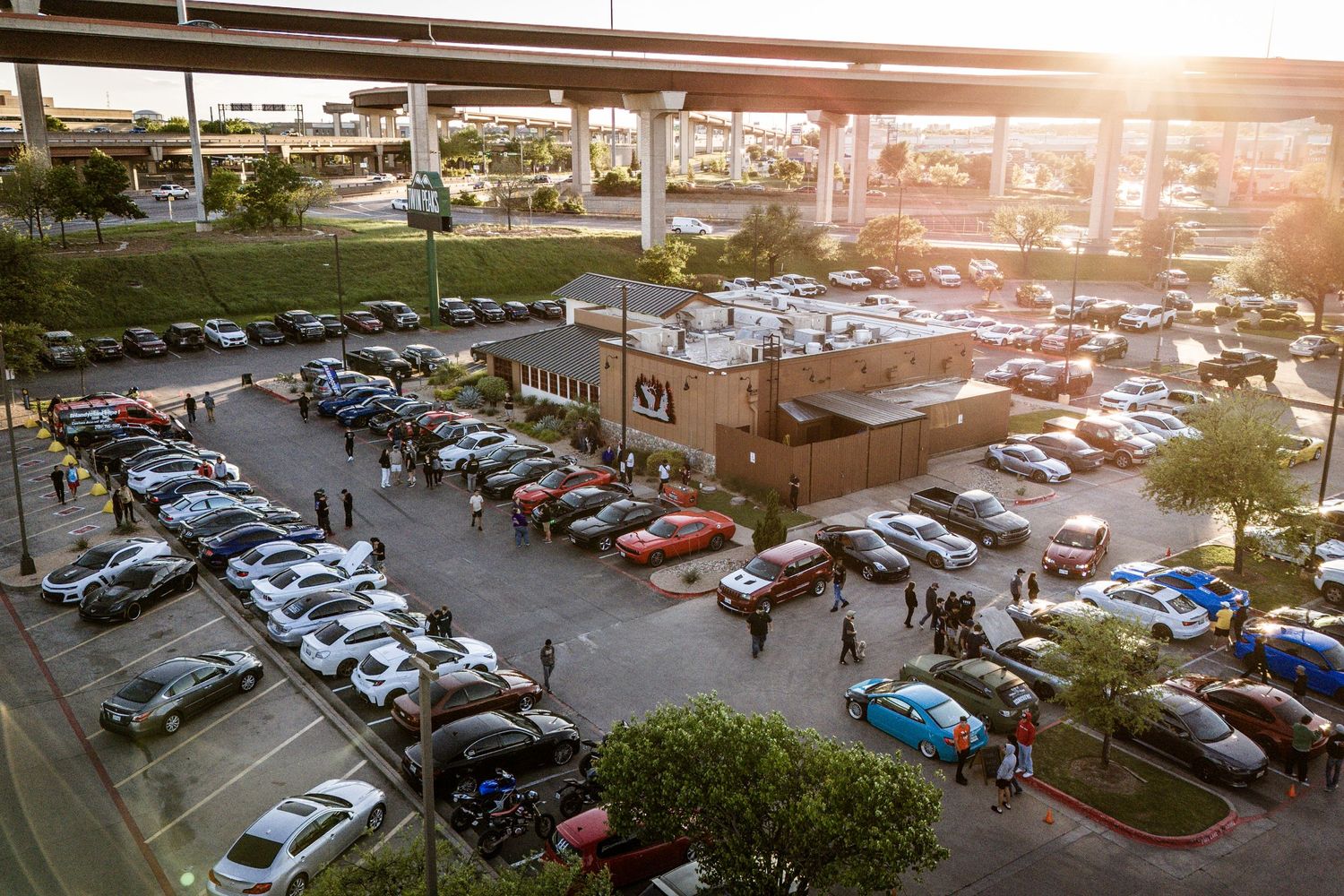 Aerial view of a crowded parking lot at sunset with cars and people gathered for an event.