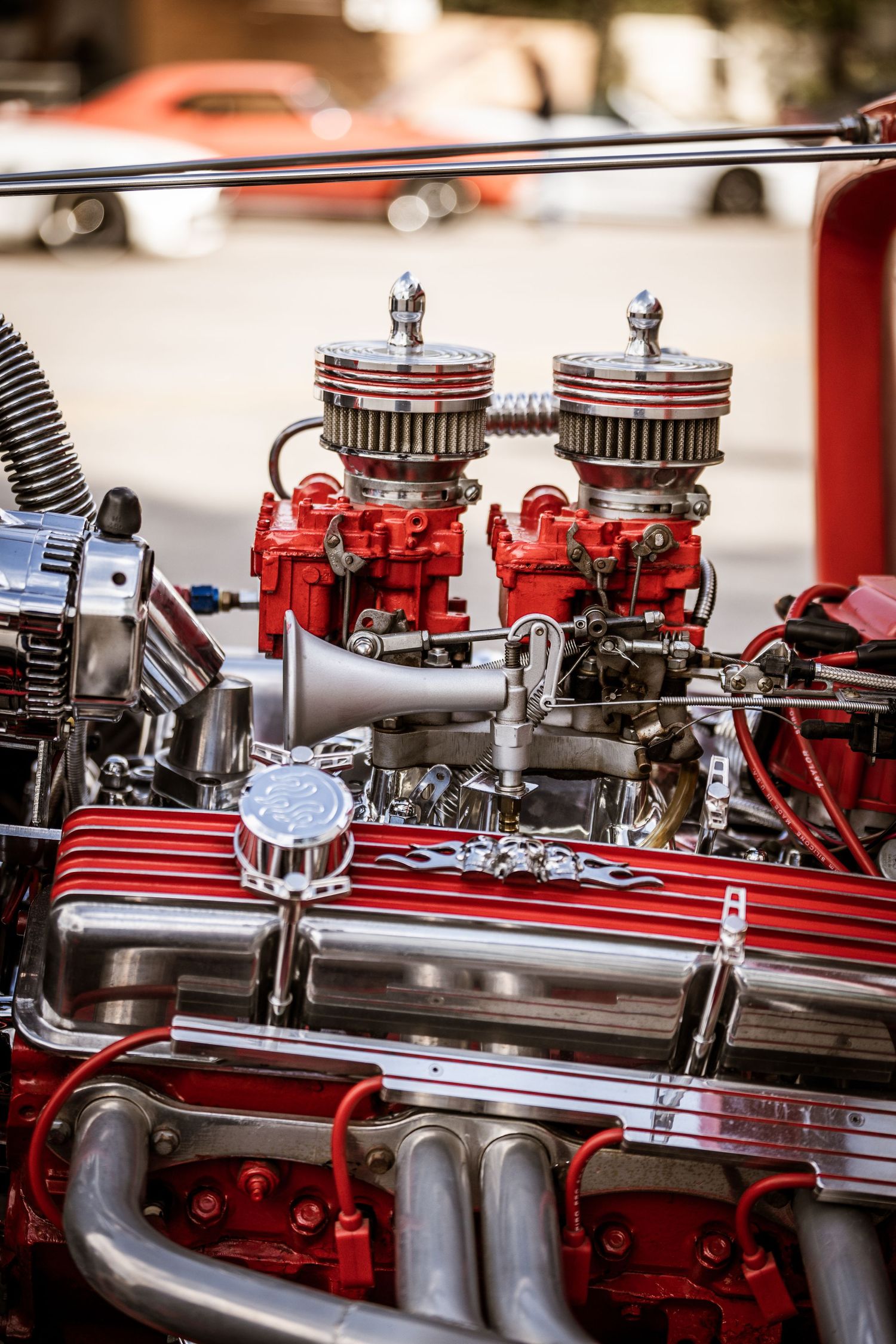 Custom red hot rod engine with dual carburetors and chrome details.