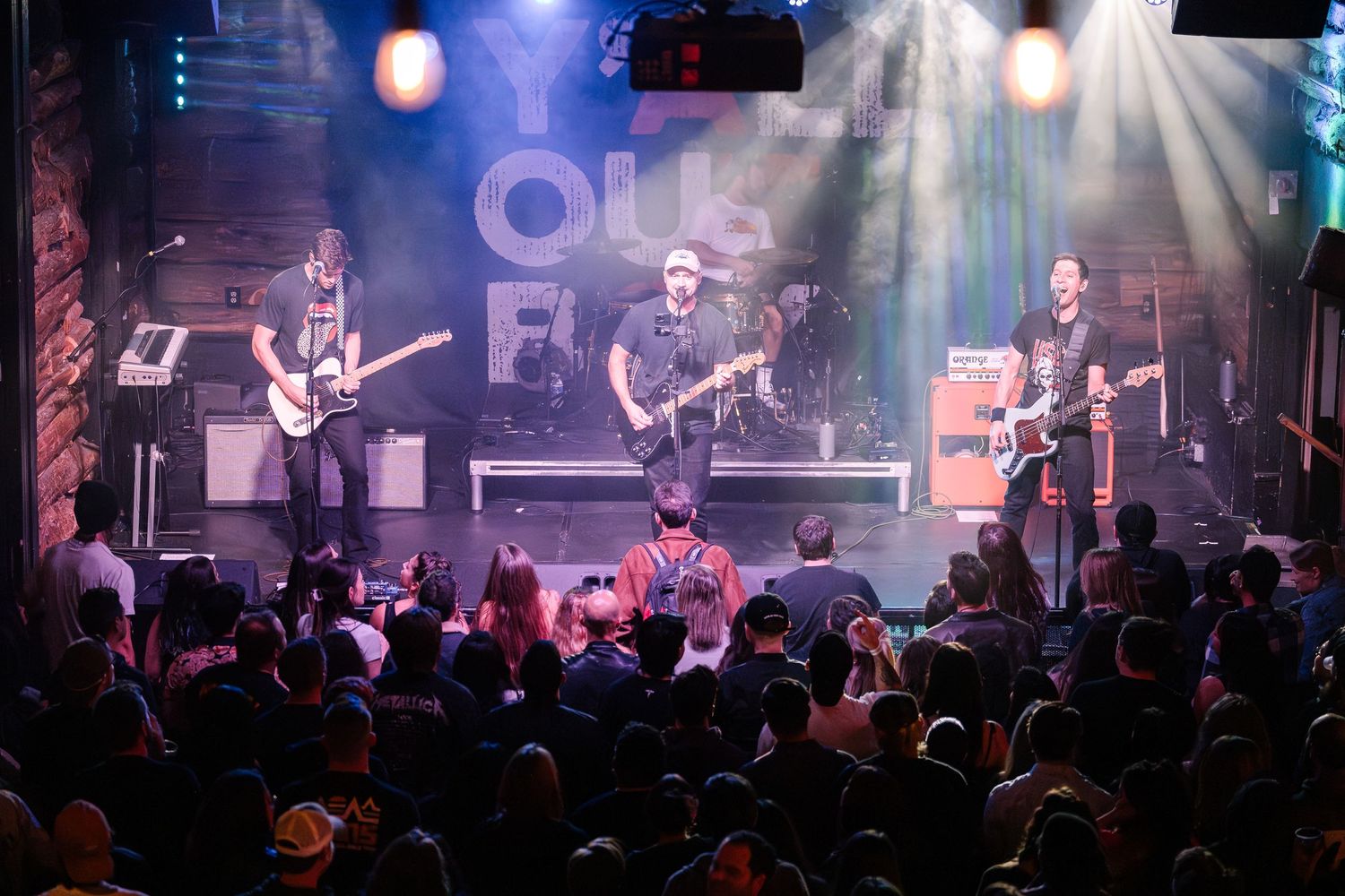 A rock band performs on stage with dramatic lighting effects as a crowd gathers below.