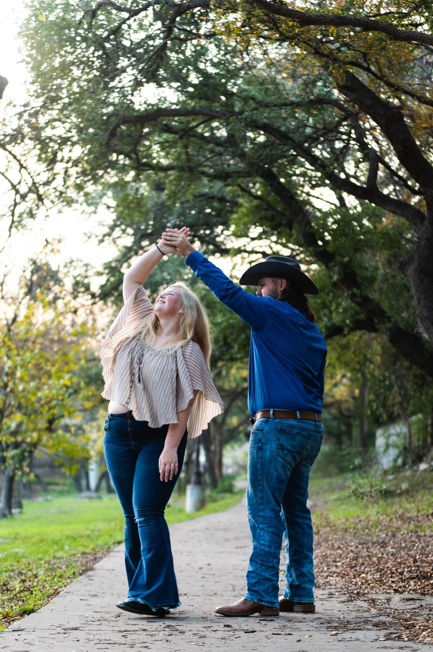 A couple dances together on a tree-lined path during an autumn photo session.