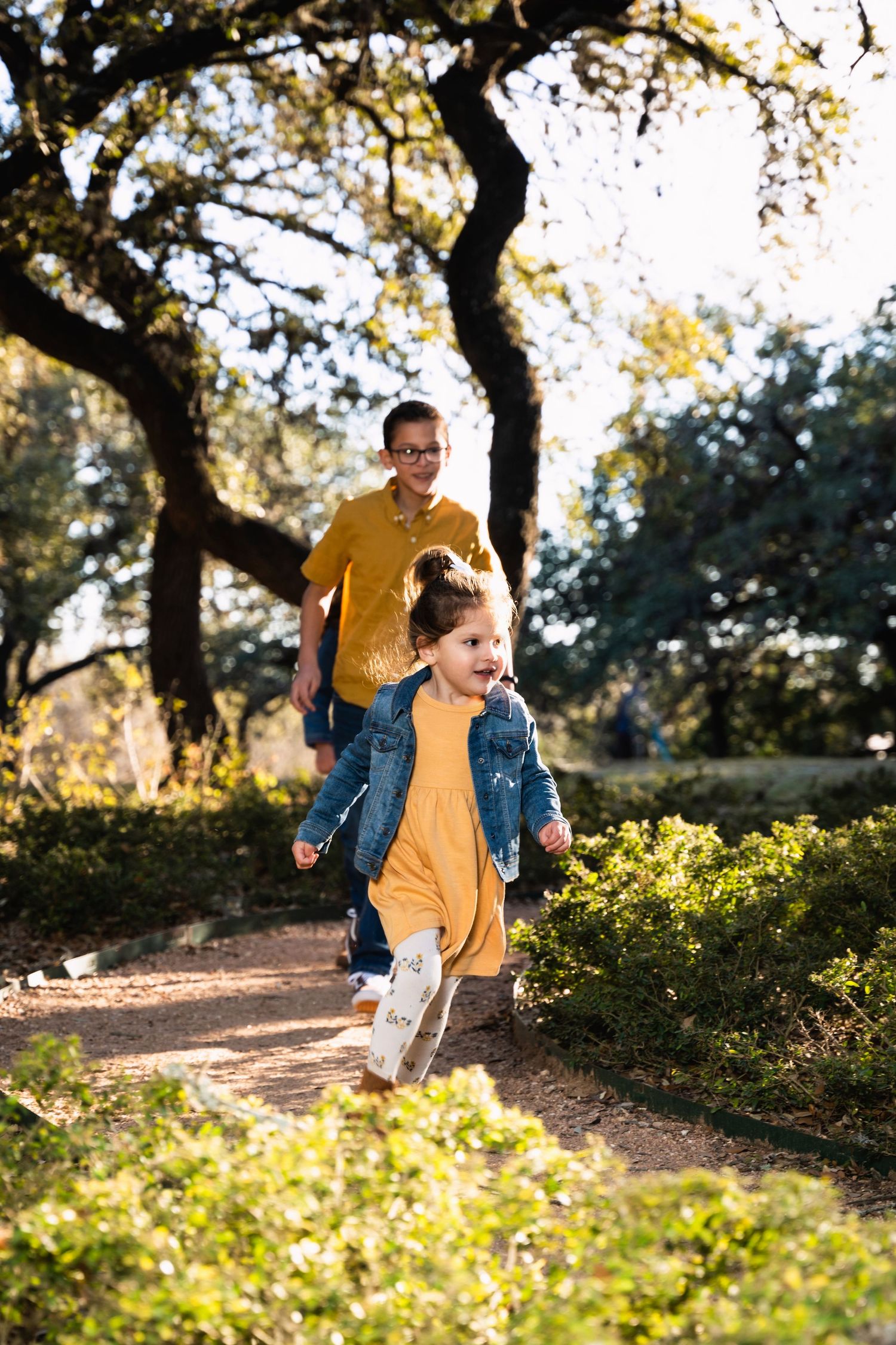 Parent and child in matching yellow shirts running on a tree-lined trail.