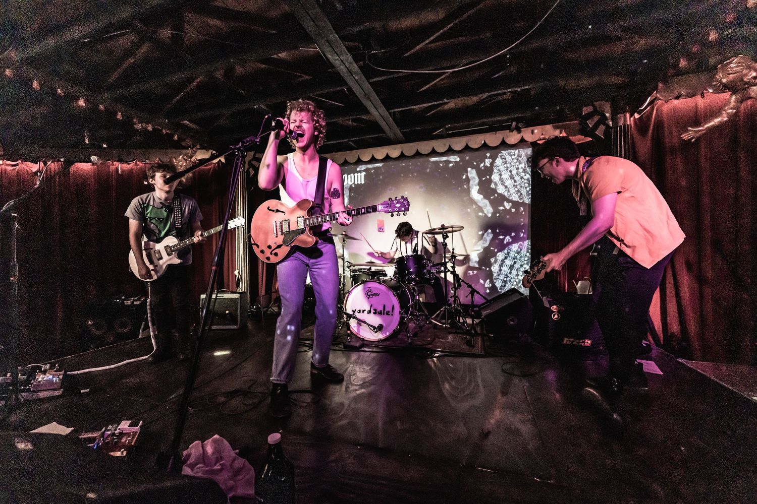 Rock band performing on dark stage with purple lighting and musical equipment.