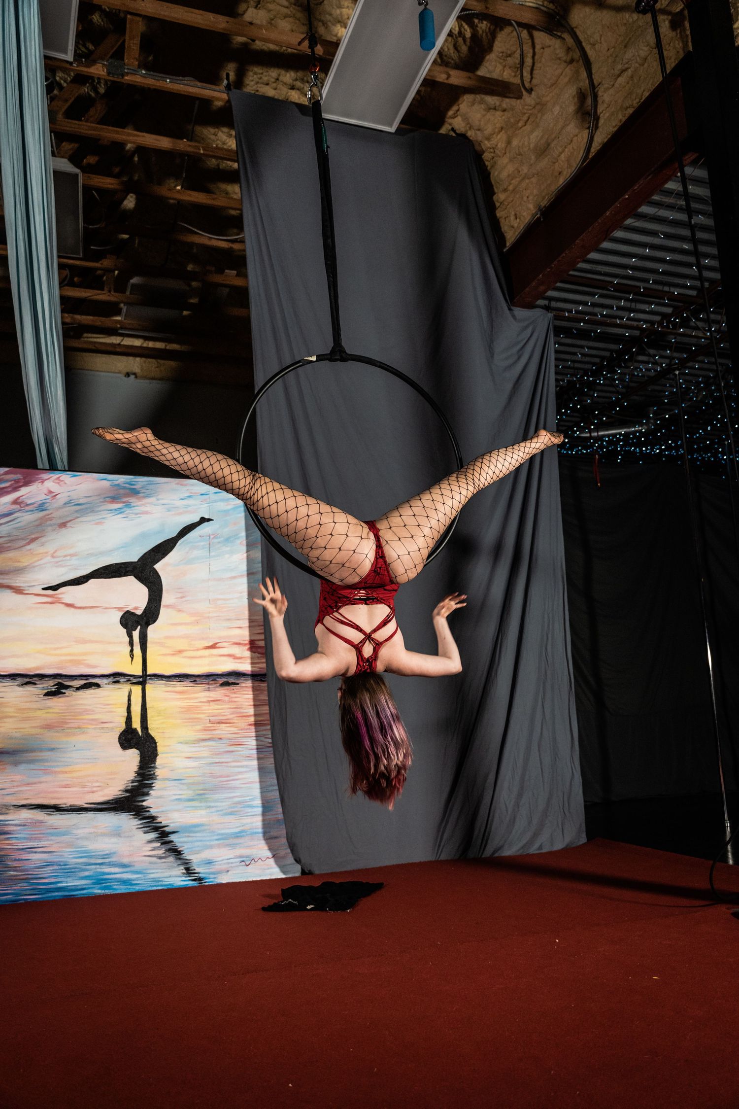 Aerial performer in red costume hanging upside down against sunset backdrop.