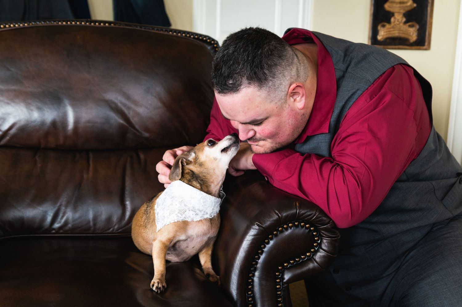Person sharing a sweet moment with their small dog on a brown leather couch.