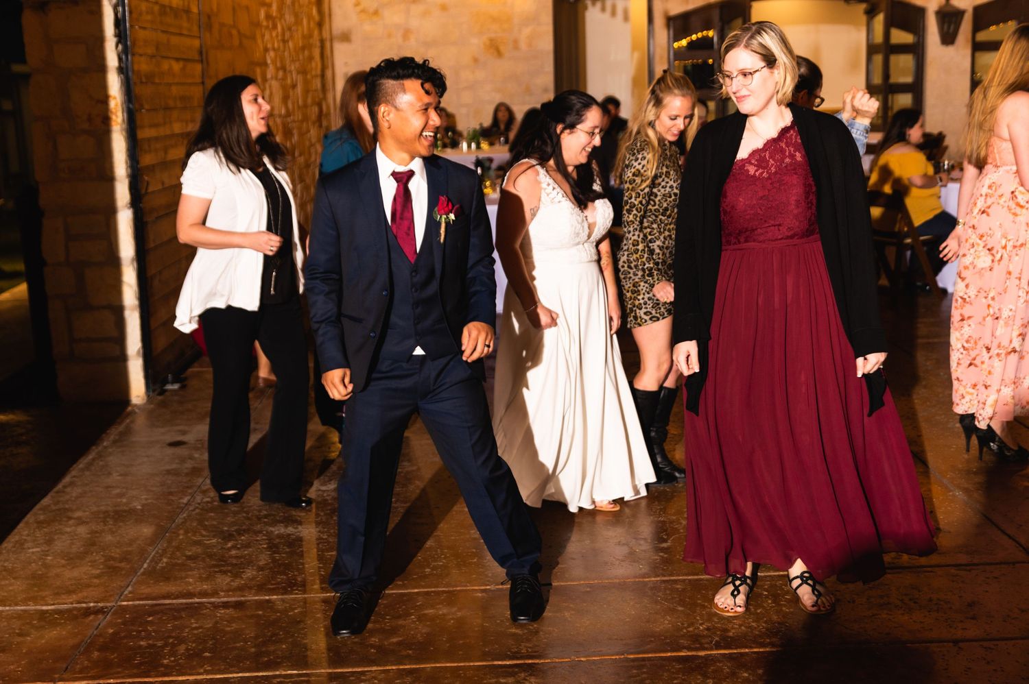 Wedding reception guests dancing and celebrating on a rustic indoor dance floor.