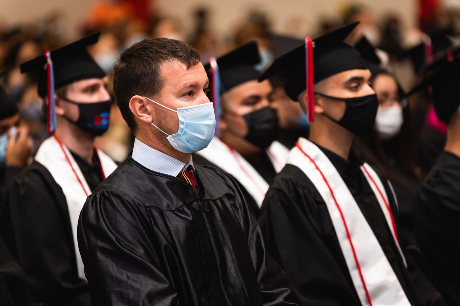 Graduates wearing protective face masks and black gowns sit during a commencement ceremony.