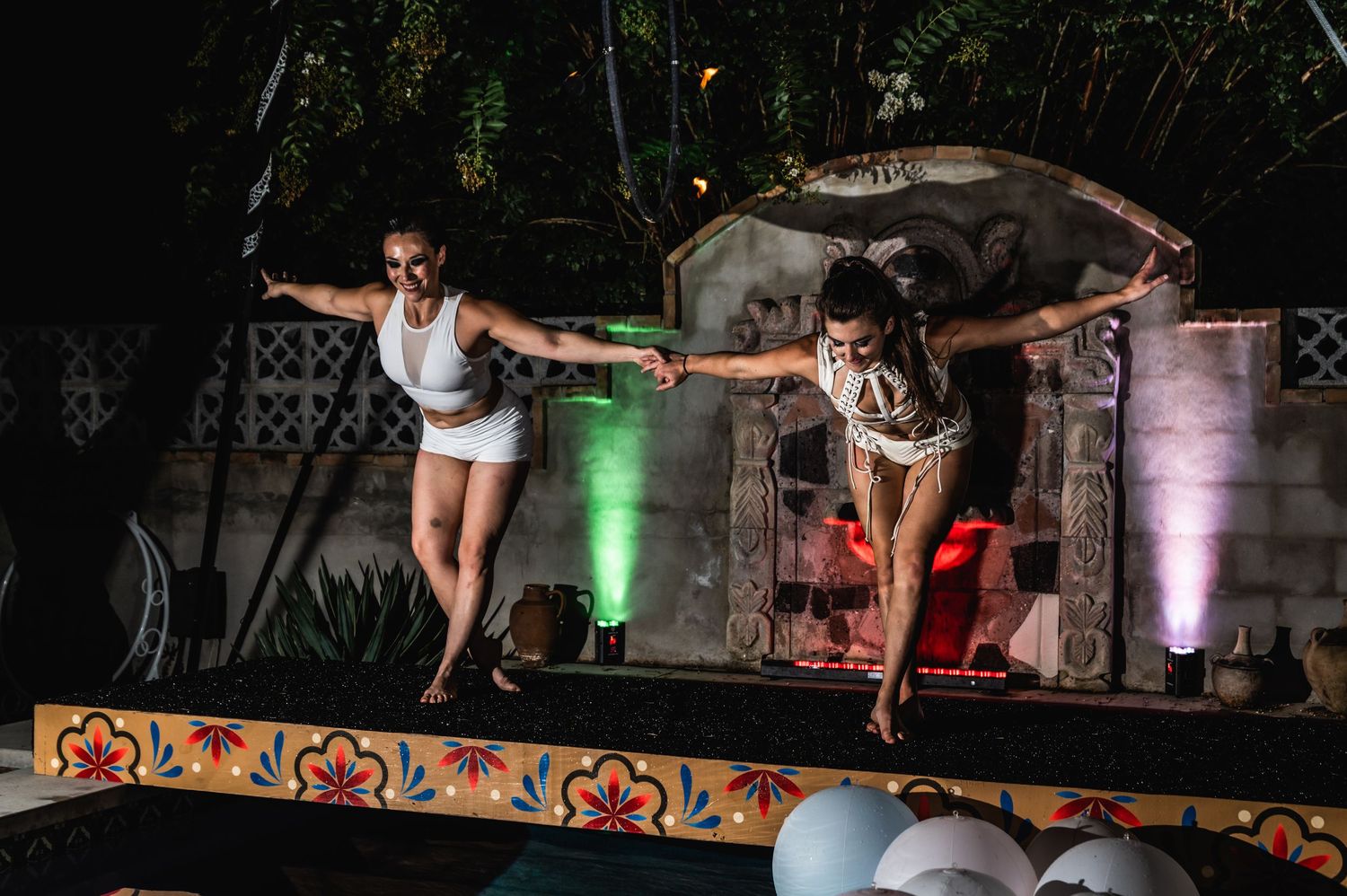Two performers strike dynamic poses during a stage show with colored lighting effects.