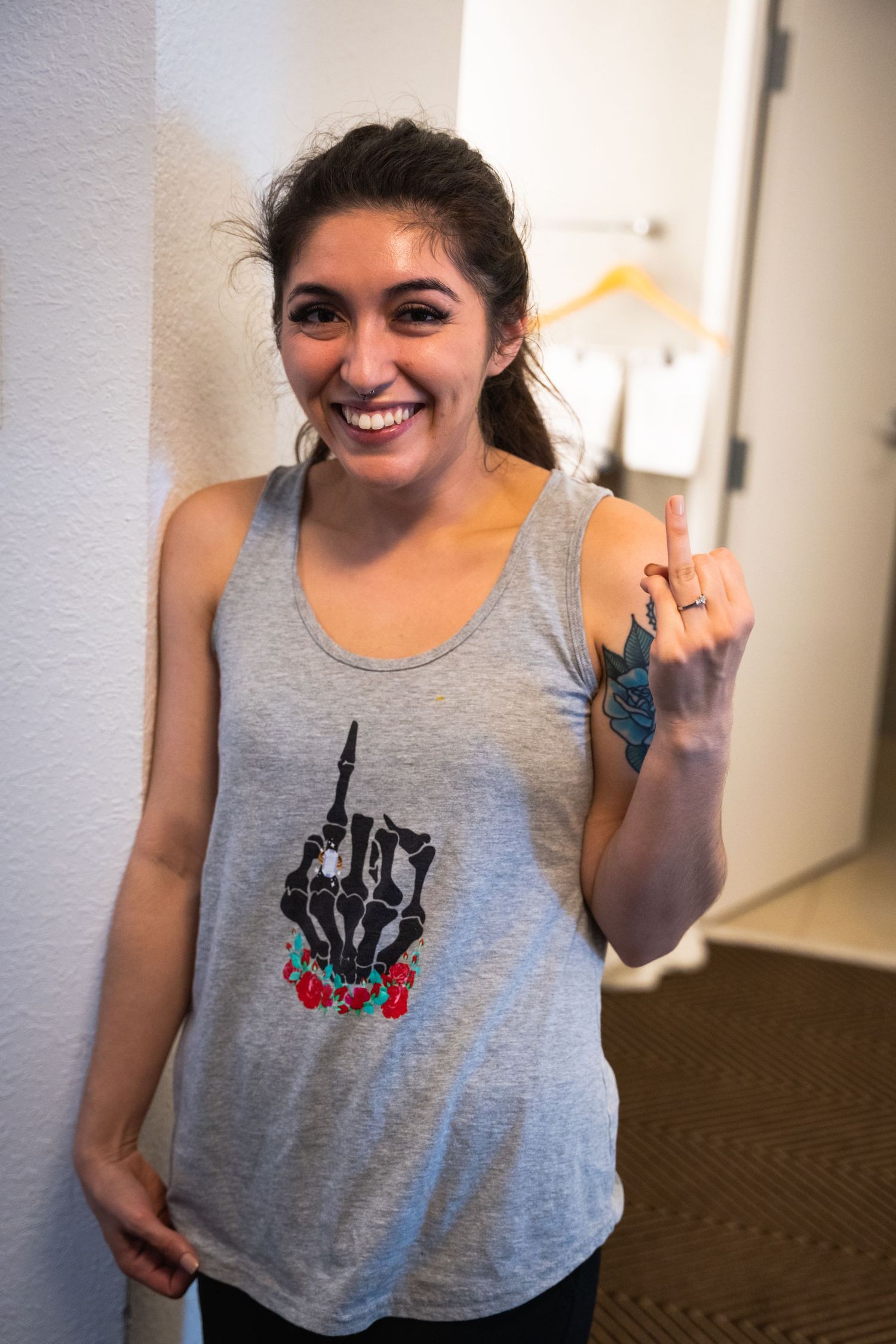 Person in grey tank top with graphic design standing against white wall.