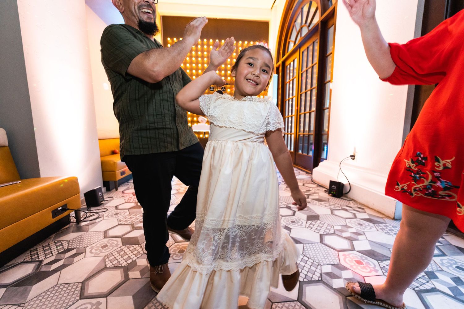 A young child in a white dress dances joyfully at a celebration.