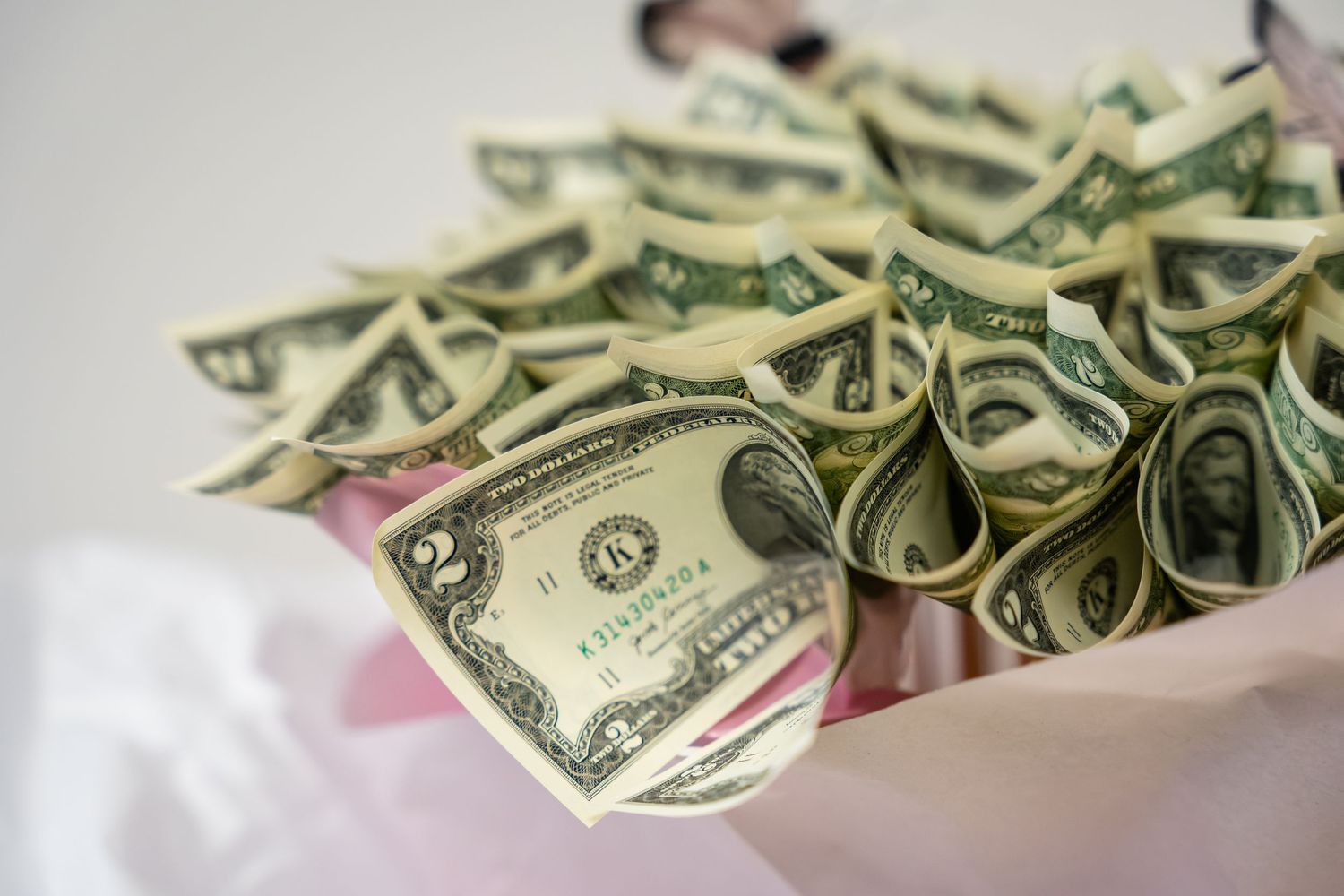 A bouquet of rolled US dollar bills arranged like flowers in a pink wrapper.