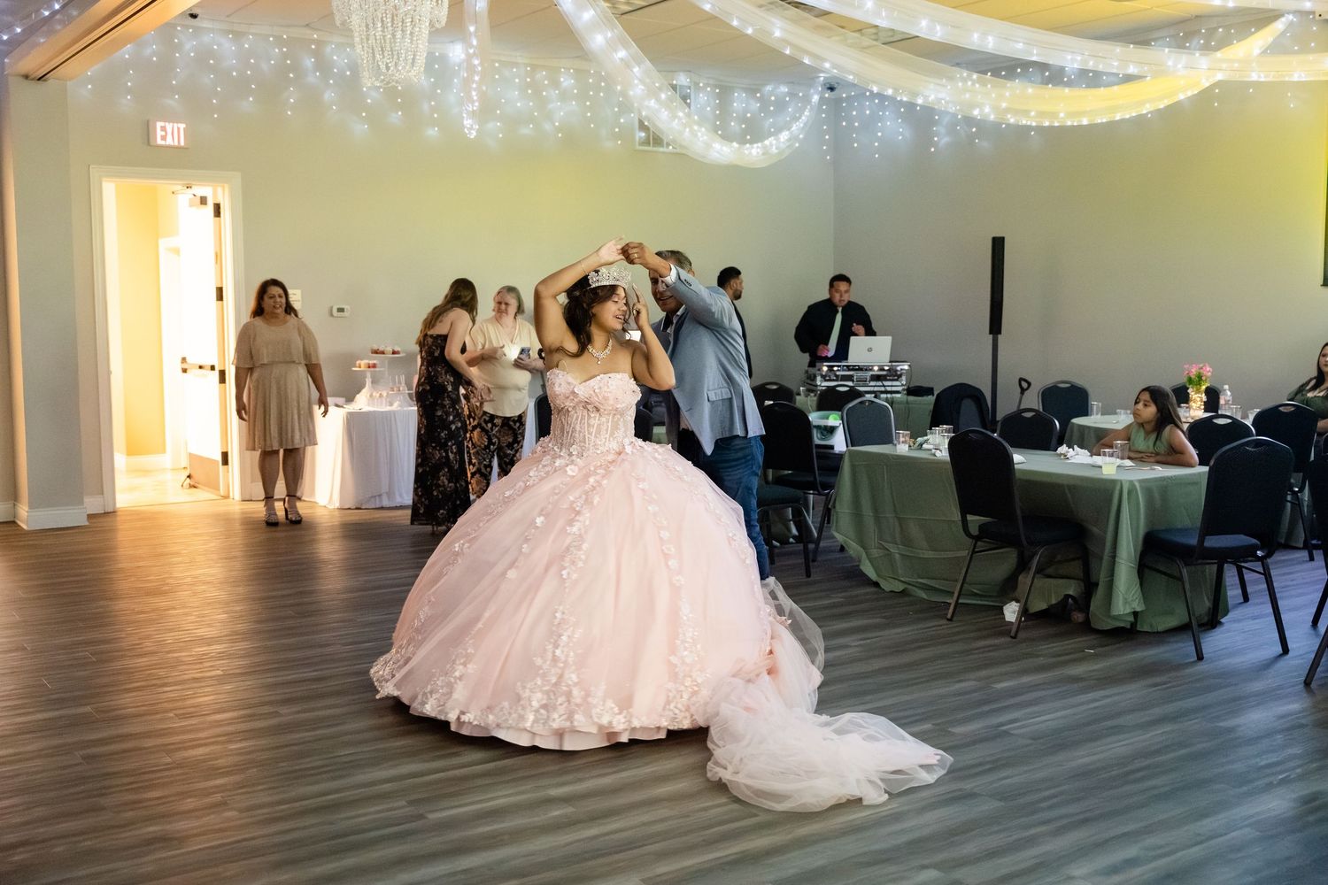 Young woman in pink ballgown dancing at quinceañera celebration in decorated banquet hall.