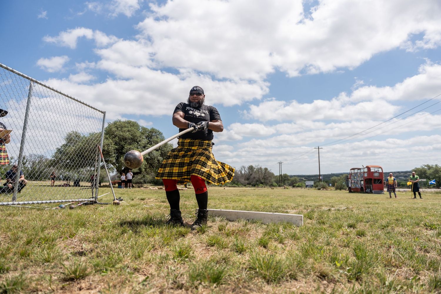 Man in tartan kilt competing in Highland Games hammer throw on sunny day.