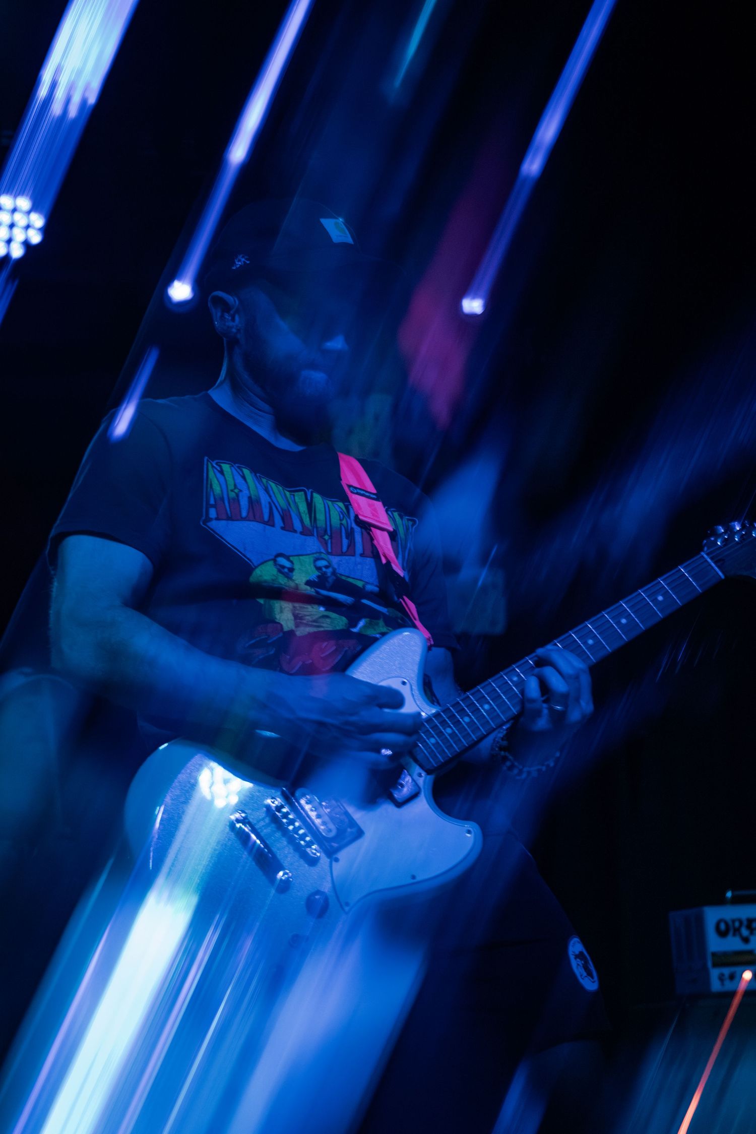 Guitarist performing on stage under vibrant blue lights, playing a white electric guitar at a live concert.