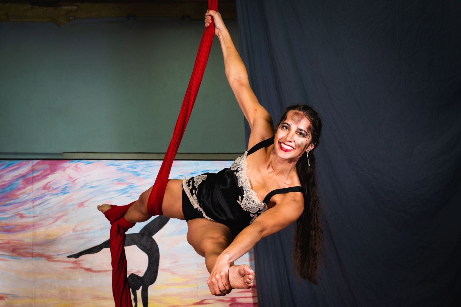 A dancer performs graceful aerial moves on red silk ribbons suspended from above.
