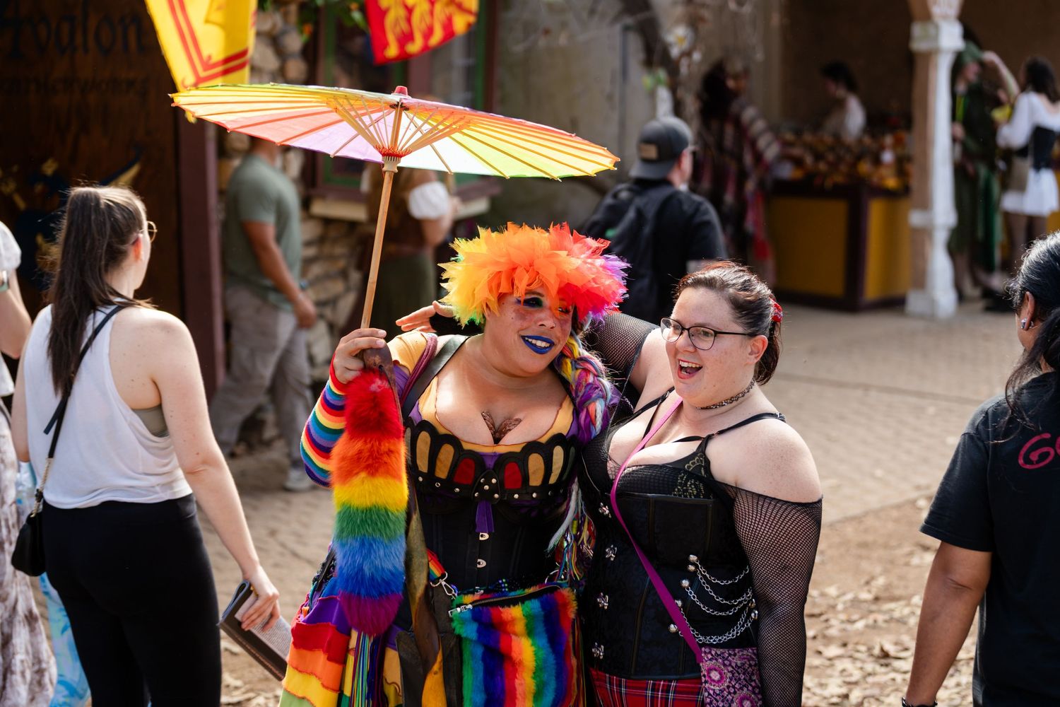 A colorful Pride parade celebration with rainbow flags, parasols and festive attendees gathering in a public space.