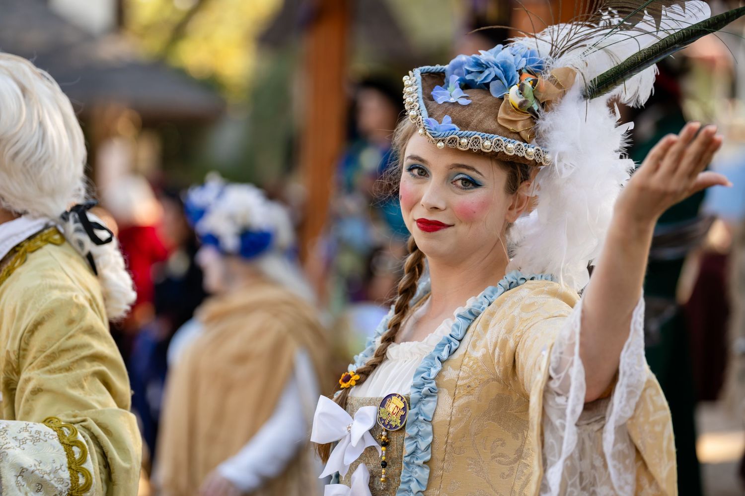 Elegant costumed participants in period dress gather at a Renaissance fair with ornate historical outfits and accessories.