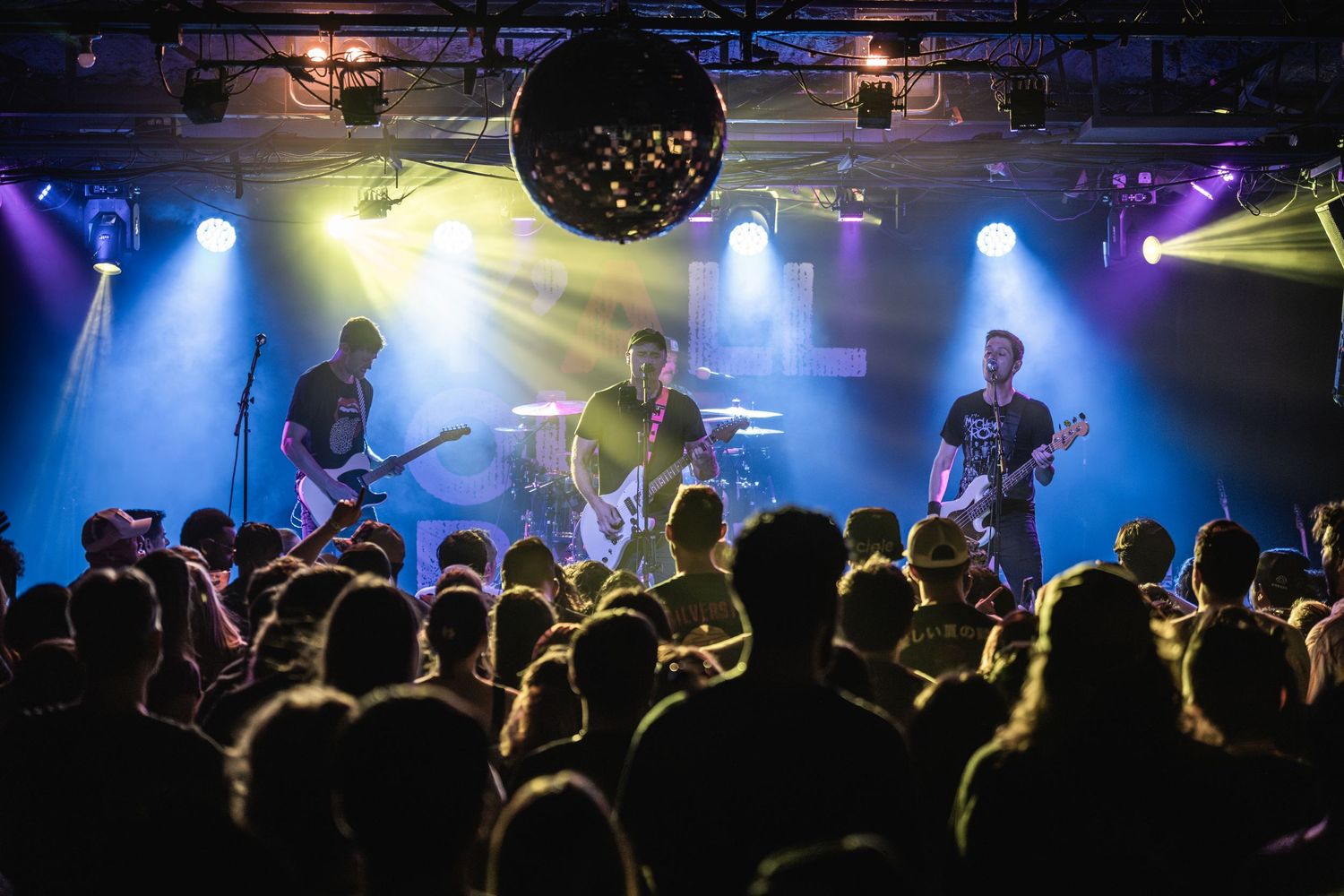 Band performs on stage with colorful lighting while crowd watches from below.