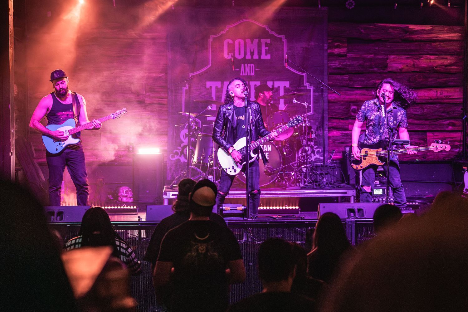 Rock band performing on stage with rustic wood backdrop and dramatic lighting.