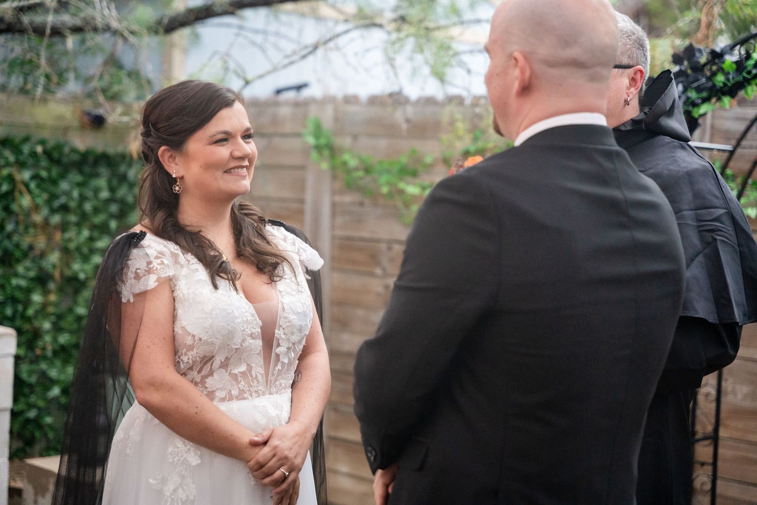 Bride in lace wedding dress smiling during outdoor ceremony.