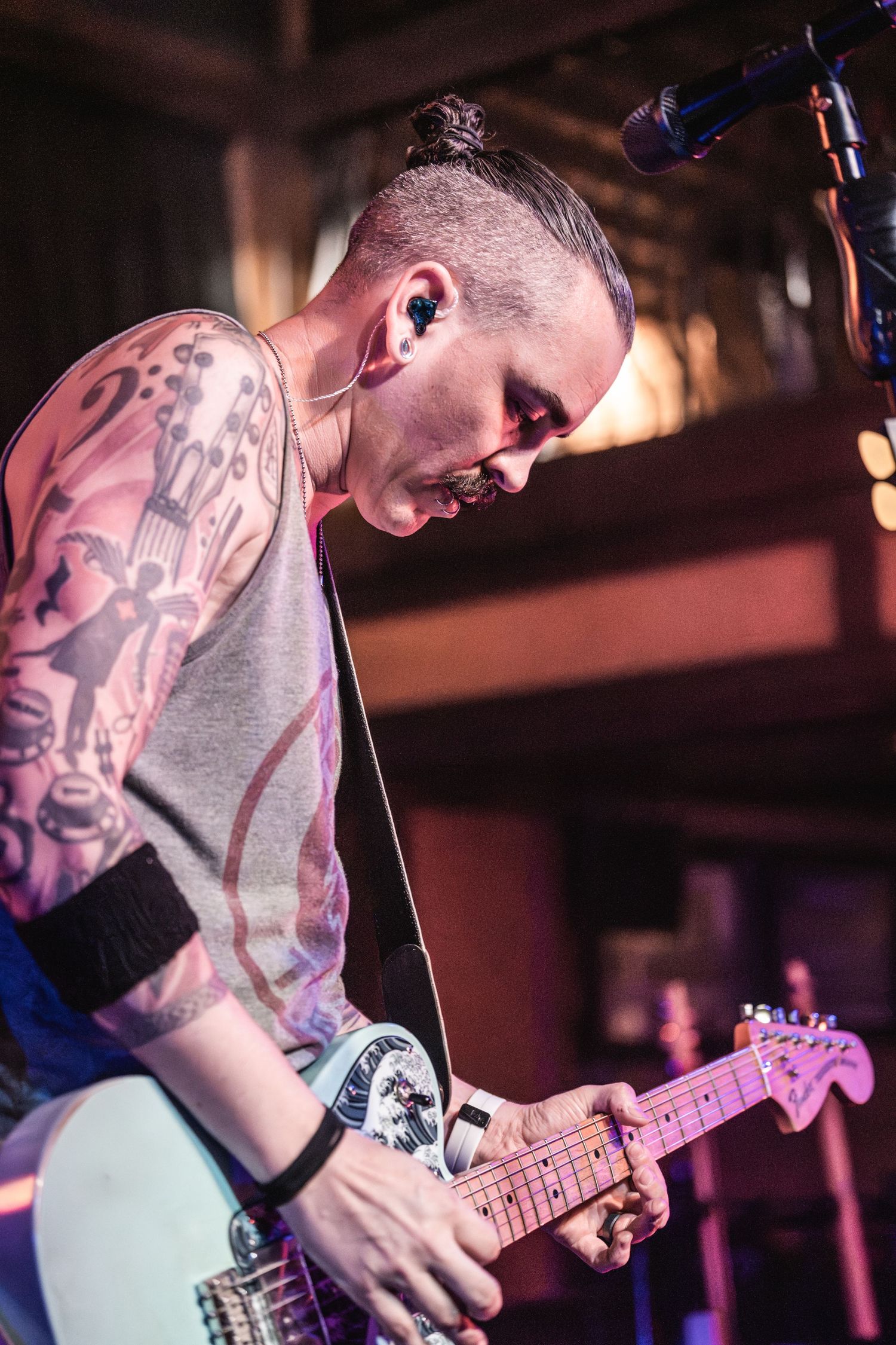 Tattooed guitarist plays mint green Fender guitar during intense performance moment.