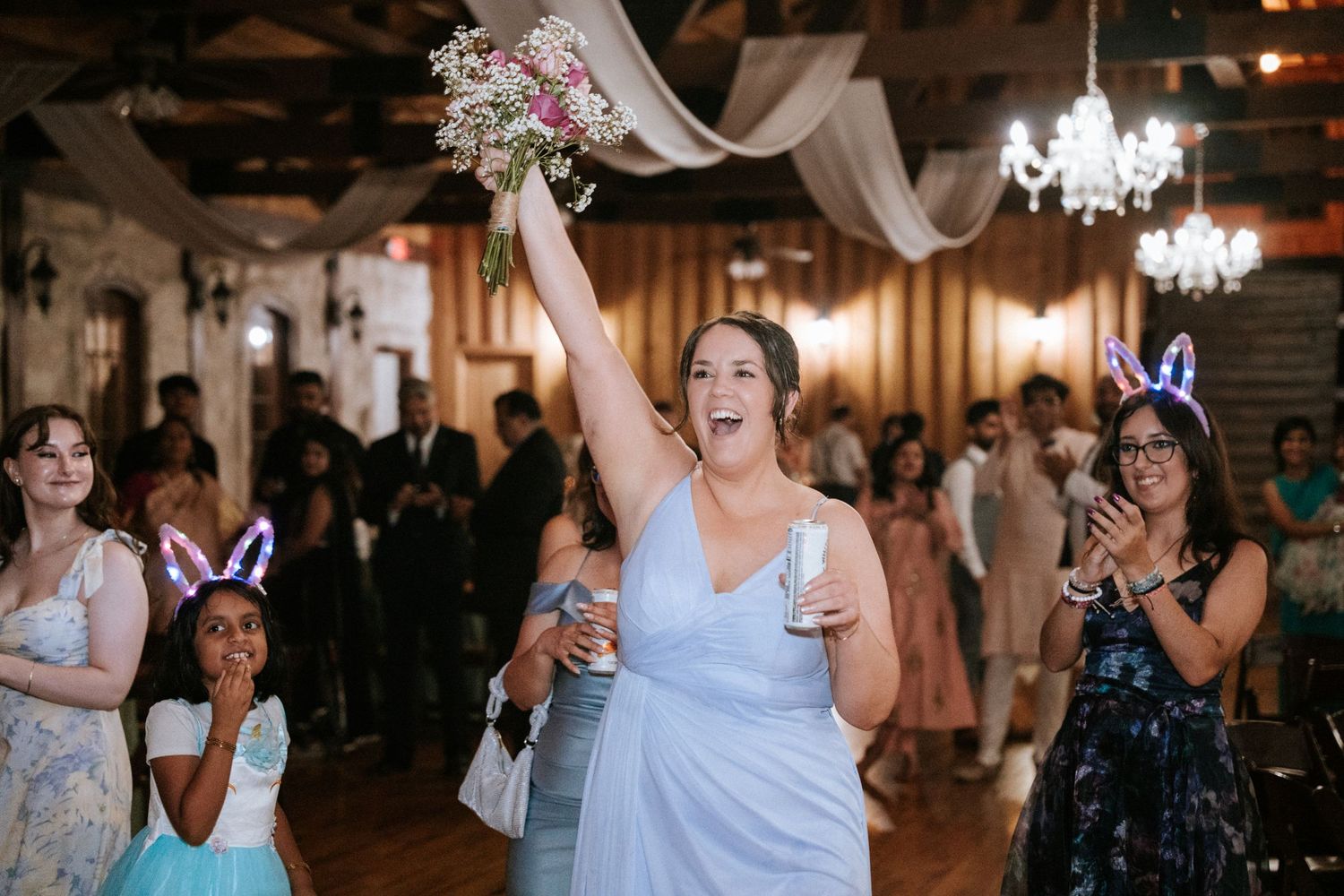 A joyful guest in a blue dress celebrates on the dance floor while holding a bouquet.