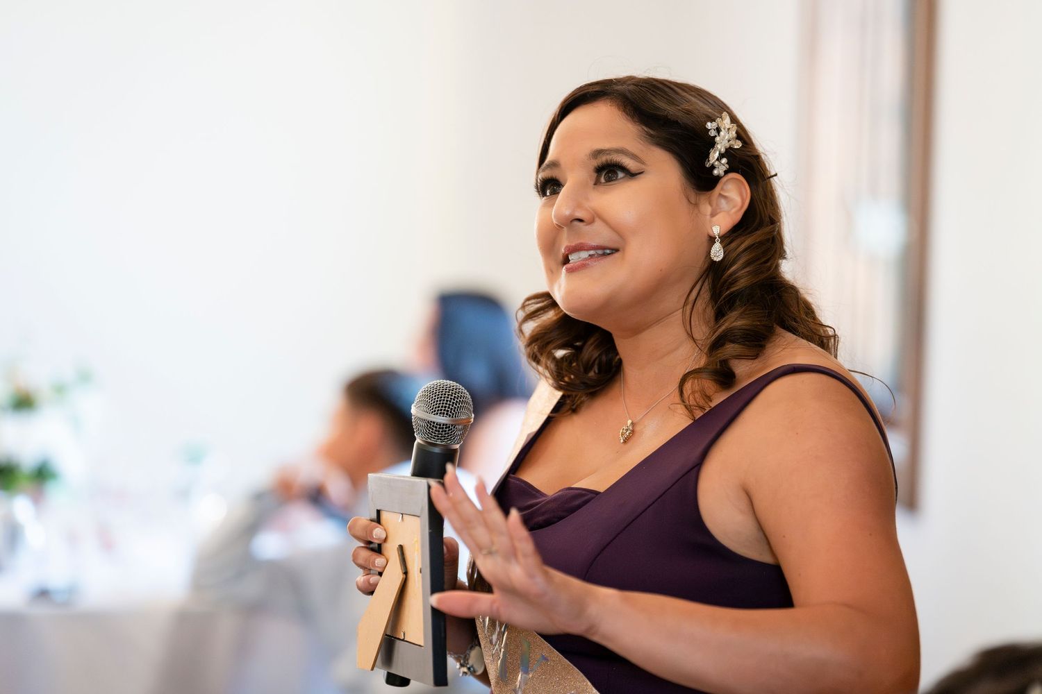 A person in a purple sleeveless dress gives a speech while holding a microphone at an indoor event.