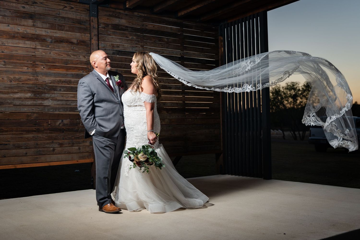 Wedding portrait with flowing veil against rustic wooden backdrop.