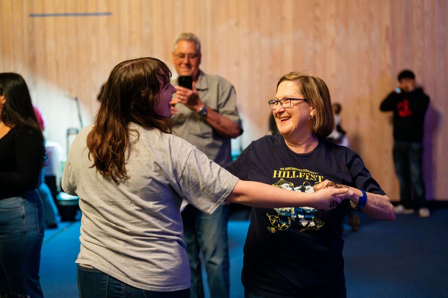 Two people greet each other enthusiastically during a social gathering in a room with blue lighting.