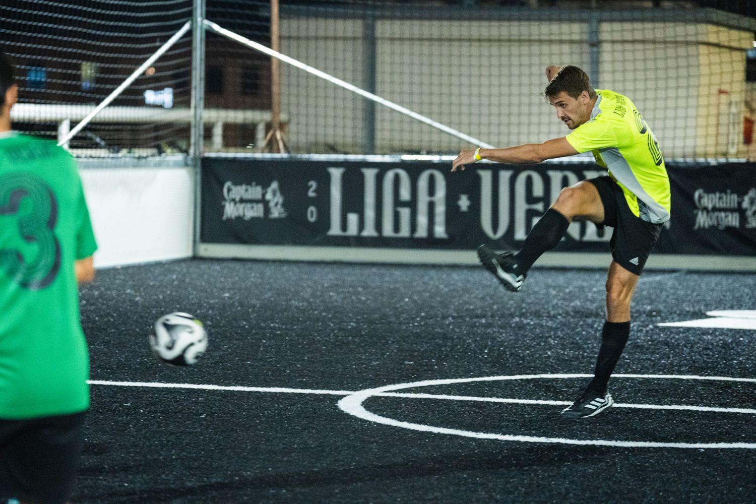Player in bright yellow uniform takes a shot during indoor soccer game.
