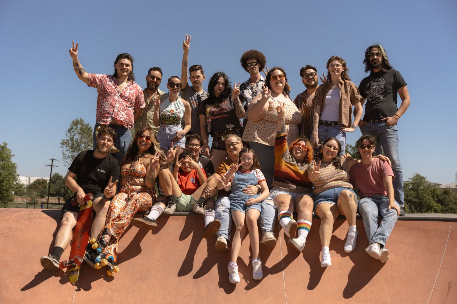 A large diverse group poses together on a ramp or skate park structure, with some sitting and others standing.