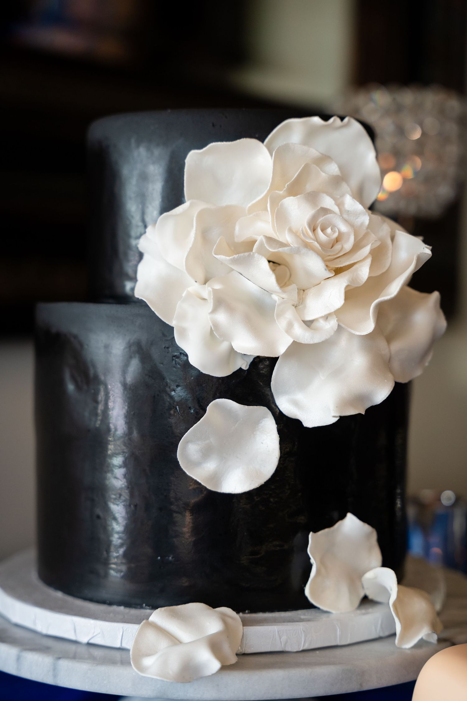 Elegant black wedding cake adorned with cascading white sugar rose petals.