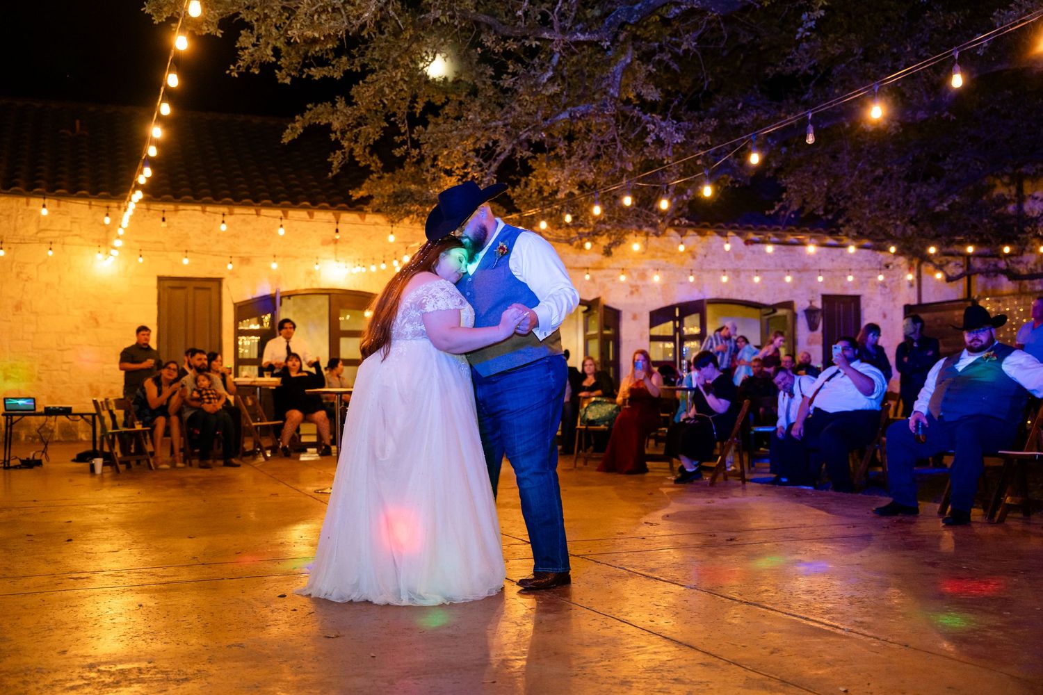 Couple dancing under warm string lights at evening wedding reception.