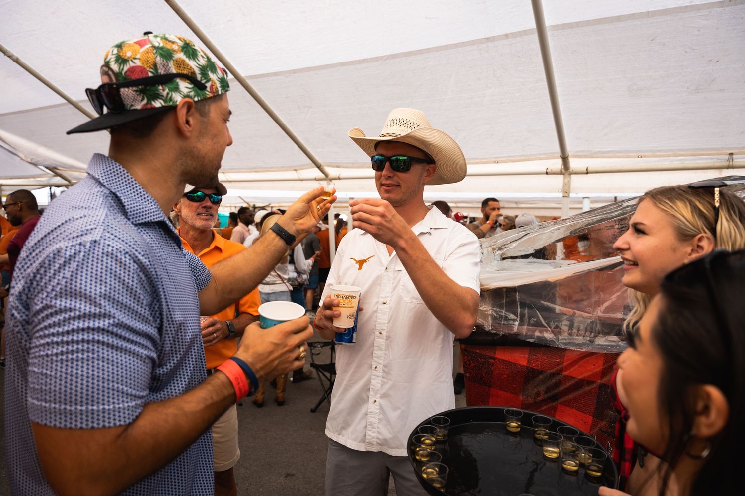 Animated conversation between tailgaters under a white tent canopy.